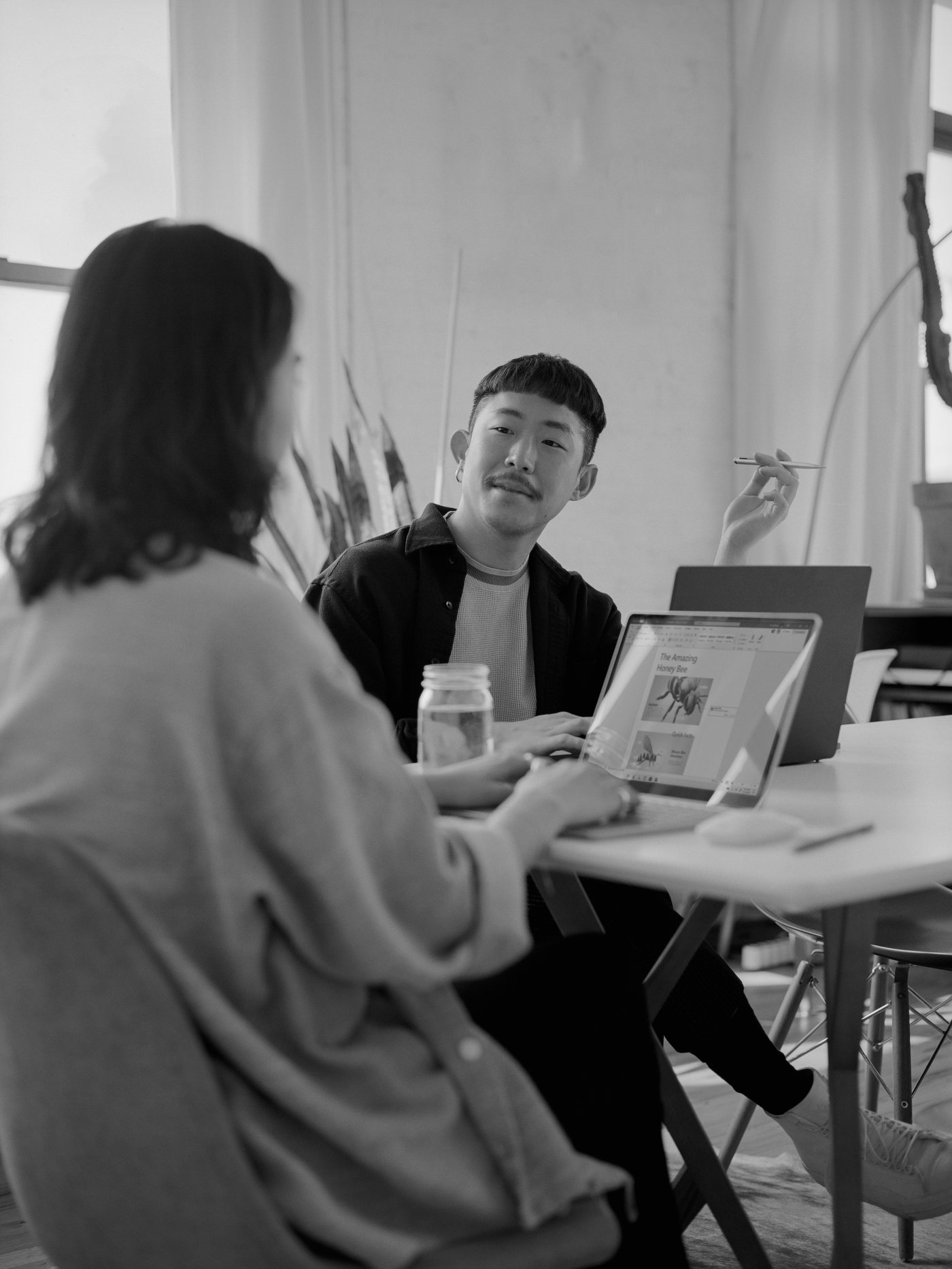 Two creatives collaborating over laptops at a table, talking through a project together.