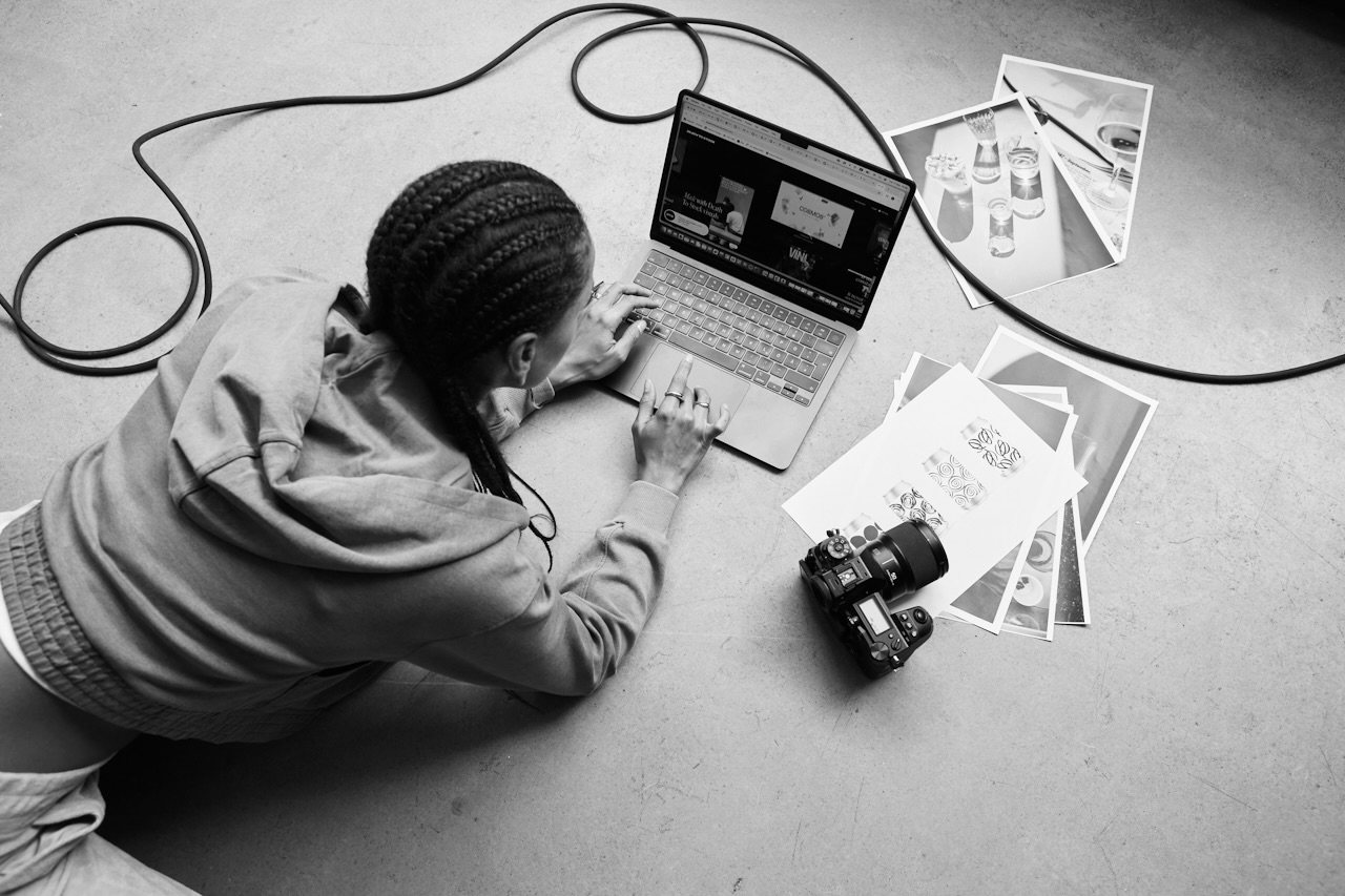 Overhead view of a photographer culling images on a laptop, with a camera and prints spread around.