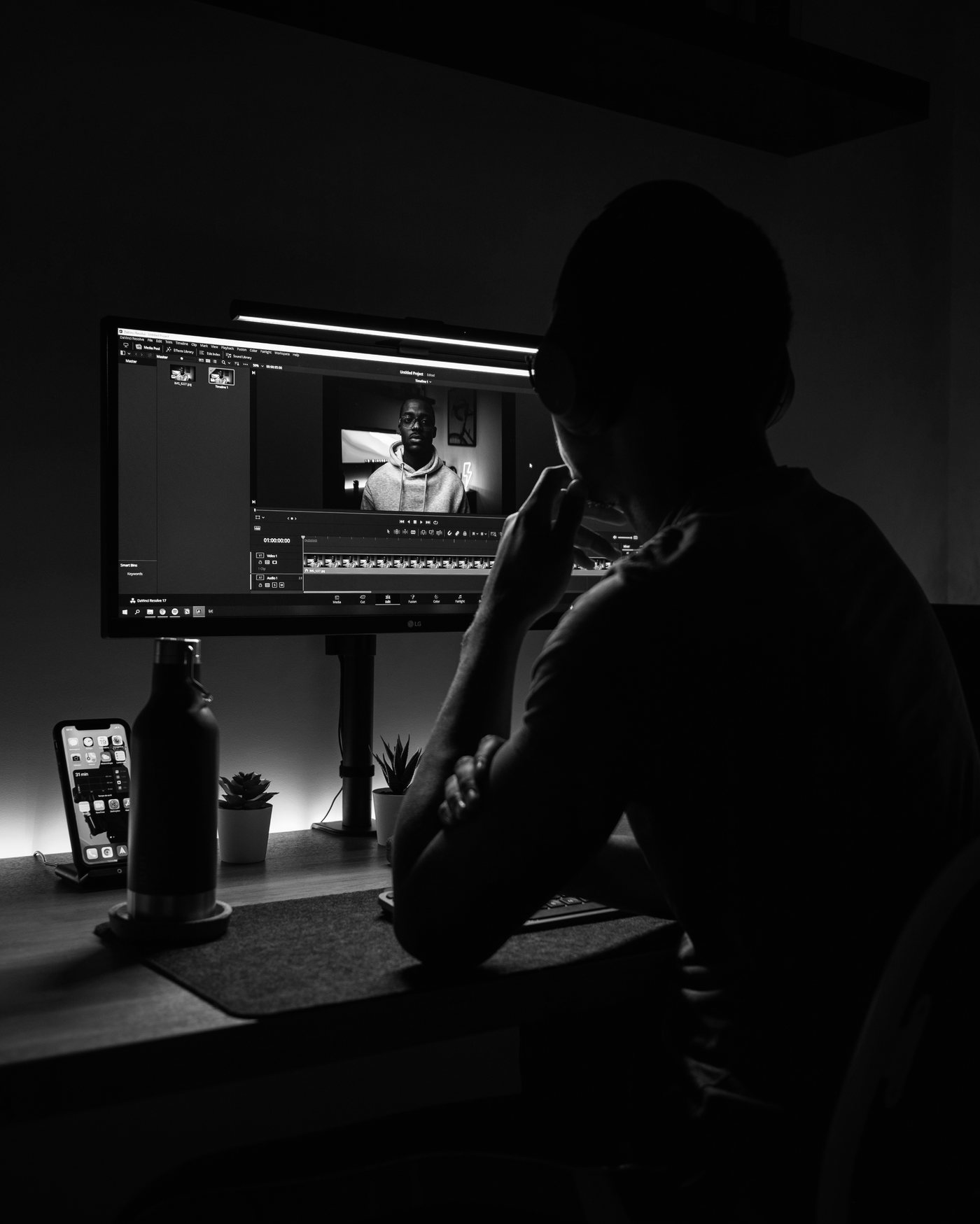 Video editor working late at a glowing monitor, cutting footage in a dark edit bay.